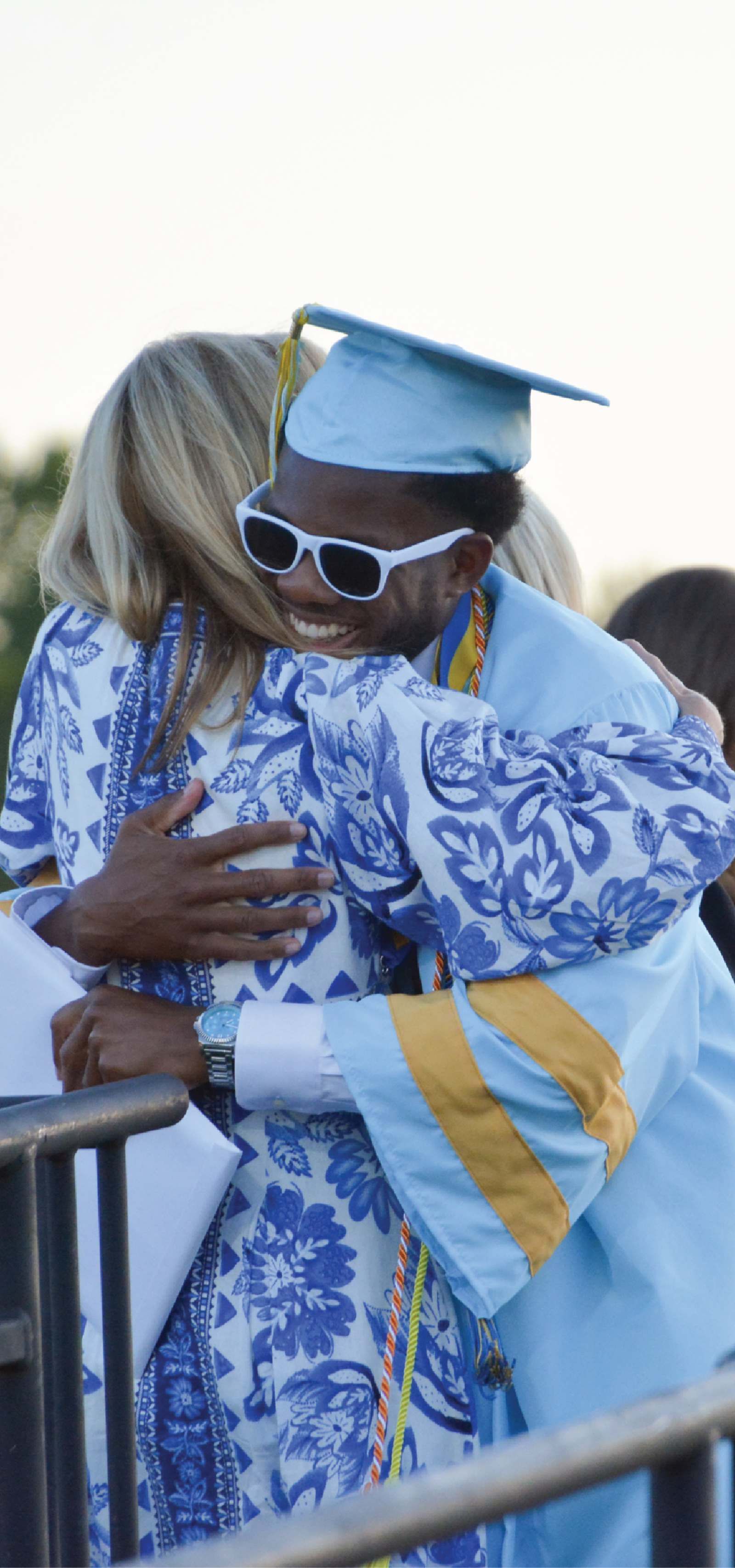 A Cape Henlopen High School graduate in a light blue cap and gown hugging a teacher